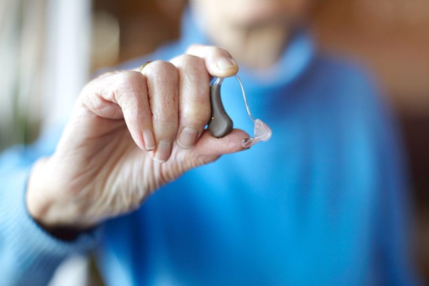 Senior person holding a behind-the-ear hearing aid before insertion.